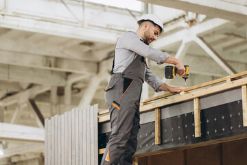 Construction worker building prefabricated modular house using cordless screwdriver