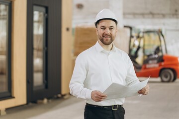 Smiling engineer holding blueprint in modular building factory