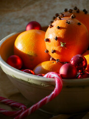 Cristmas decorations. Christmas crafts. Oranges decorated with carnation, laying in a porcelain bowl with red tree decorations and candy canes. Smells great. 