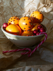 Cristmas decorations. Christmas crafts. Oranges decorated with carnation, laying in a porcelain bowl with red tree decorations and candy canes. Smells great. 