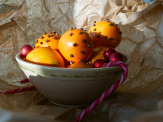 Cristmas decorations. Christmas crafts. Oranges decorated with carnation, laying in a porcelain bowl with red tree decorations and candy canes. Smells great. 