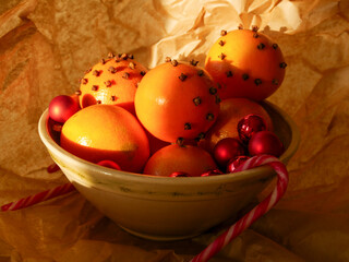 Cristmas decorations. Christmas crafts. Oranges decorated with carnation, laying in a porcelain bowl with red tree decorations and candy canes. Smells great. 