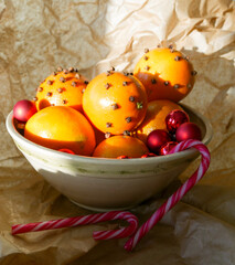 Cristmas decorations. Christmas crafts. Oranges decorated with carnation, laying in a porcelain bowl with red tree decorations and candy canes. Smells great. 