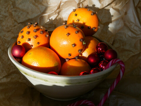 Cristmas decorations. Christmas crafts. Oranges decorated with carnation, laying in a porcelain bowl with red tree decorations and candy canes. Smells great. 