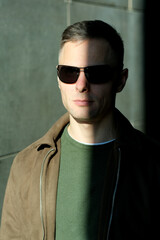 Man in sunglasses stands confidently in sunlight against a textured wall