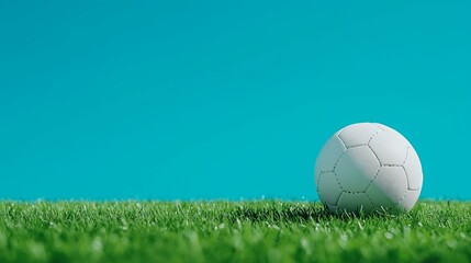 Fototapeta premium A White Soccer Ball Rests on Lush Green Artificial Turf Against a Vibrant Blue Background