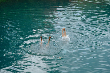 Two swimmers diving into a calm lake, legs up.
