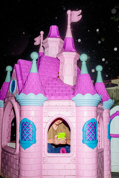 Funny picture with a teenager and a smartphone inside a toy castle