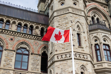 Close-up of the Canadian flag waving near the Parliament building in Ottawa, highlighting the intricate Gothic Revival stonework and rich national heritage