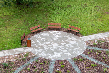 A circular seating area with wooden benches surrounded by green grass and garden beds.
