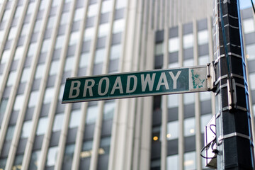 A close-up view of a Broadway street sign in New York City, with a background of modern office building windows.