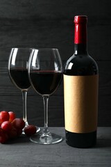 Bottle of red wine with grapes and glasses on wooden background