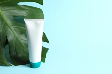 Cosmetic tube with monstera leaf on color background