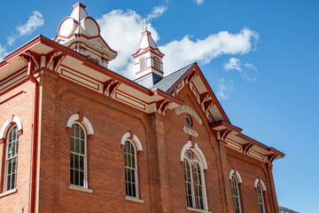 Historic red brick schoolhouse from 1874 featuring intricate architecture and arched windows under a clear sky.
