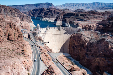 Aerial view of Hoover Dam with winding canyon road and Lake Mead in the background