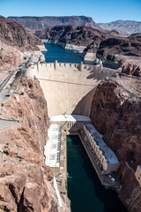 Aerial view of Hoover Dam, Colorado River, and surrounding rugged canyon landscape under clear blue skies