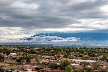 A view of Albuquerque neighborhoods with the Sandia Mountains under cloudy skies.
