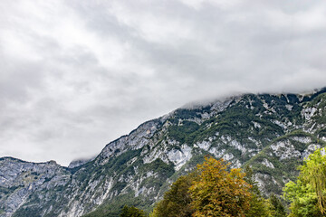 A mountain range covered in mist with forested slopes and rocky textures, surrounded by lush greenery