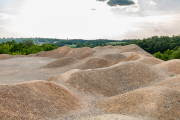 Rolling sand hills near a quarry, blending earthy tones with lush green fields and a serene afternoon sky