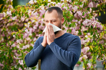 Man allergic suffering from seasonal allergy at spring in blossoming garden at springtime. Man...