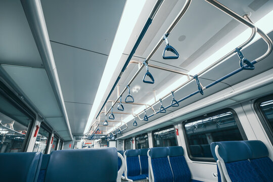 Interior of an empty train with blue seats and overhead handrails