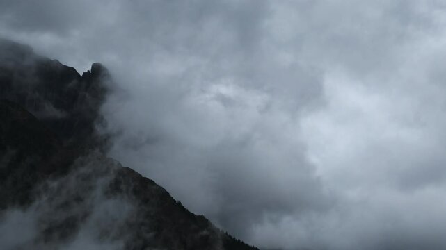 Time lapse of gray storm clouds blowing across a rocky mountain with distant trees
