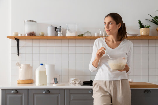 Woman holding whisk and bowl is making a cake in a modern kitchen