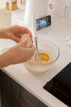 Woman cracking egg into batter while watching online cooking show 