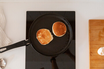 Two pancakes frying in pan on black stovetop