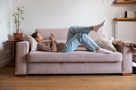 Young woman relaxing on sofa using mobile phone at home