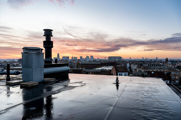 Shiny surface of a flat rooftop with chimneys and the sunset of the city in the background,...