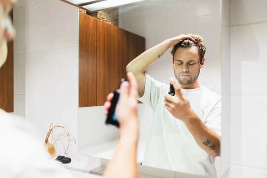 Man Using Health Spray in Front of Mirror in Bathroom