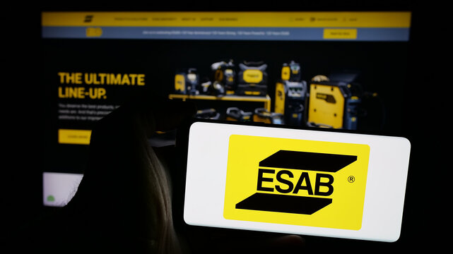 Stuttgart, Germany - 11-07-2024: Person holding mobile phone with logo of industrial company ESAB Corporation on screen in front of business web page. Focus on phone display.