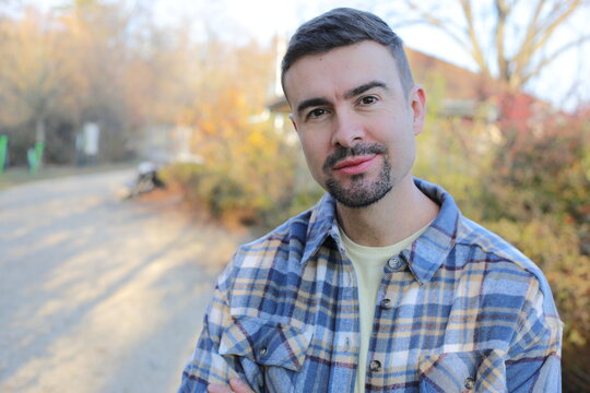 Confident Man in Plaid Shirt Standing Outdoors in a Park at Sunset