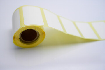 Roll of Blank Adhesive Labels on White Background. A roll of blank rectangular adhesive labels with yellow backing, laid on a white surface, ready for customization or printing.

