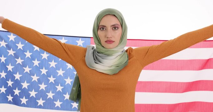 Young woman in hijab raises national American flag on white background. Arab female expresses proudness of United States citizenship