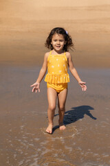 Happy caucasian toddler girl walking on sandy beach in California, summer vacation and childhood memories concept