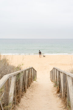 Man with backpack walking dog on empty beach towards ocean