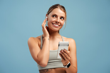 Positive fit young woman listening the music with headphones holding mobile phone in studio