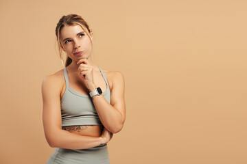 Pensive pretty sporty woman posing in studio over beige background, copy space