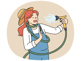 Clumsy woman with garden hose accidentally sprays herself with water while watering backyard lawn during drought. Girl got tangled in garden hose due to failure or lack knowledge of safety precautions