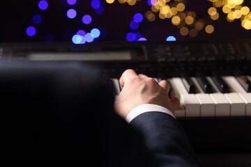 Man playing piano against blurred lights, closeup. Bokeh effect