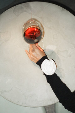 A hand elegantly holds a glass of red wine on a marble table
