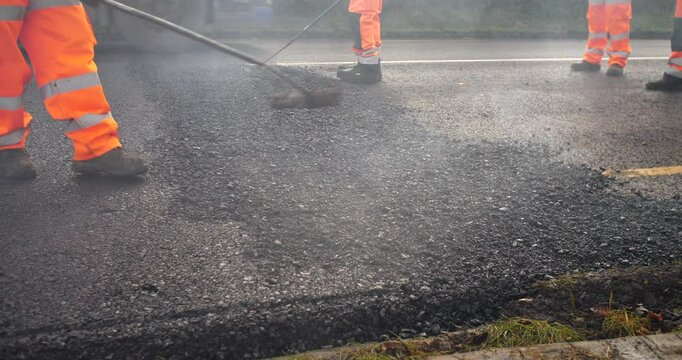 Road workers rake freshly laid hot asphalt tarmacadam
