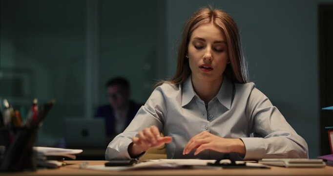 Fatigued woman office clerk watches on time on smartphone and lies down onto desk. Overworked lady feels strong stress of toxic work environment