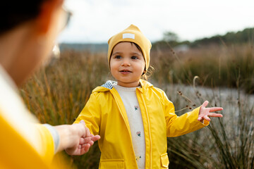 Mom holding hand of her baby girl with a yellow raincoat