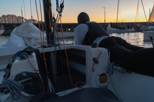 Man lying on sailboat at dusk with sails and other boats in view