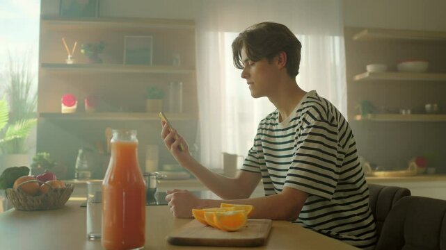 Cheerful young Caucasian man holding yellow smartphone in hands and looking at screen of gadget. Happy guy reading messages in kitchen. Tracking moving around. Indoors. Parallax effect