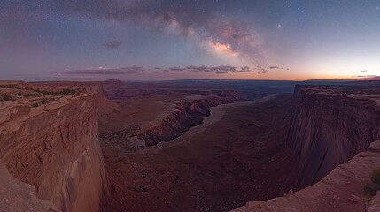 A stunning panoramic view of a canyon under a starry sky at dusk.
