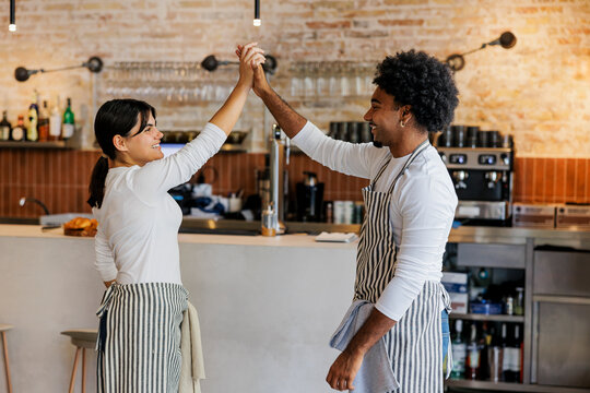 Two young cafe workers giving high five at coffee shop